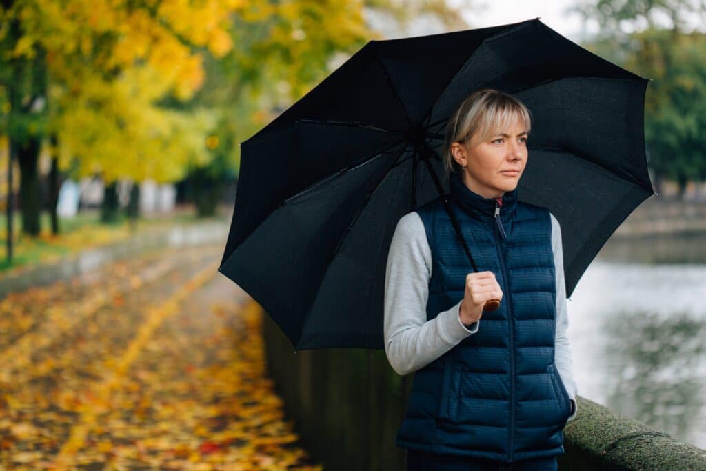 Pretty young blonde sad woman with umbrella in waistcoat in colorful autumn park.
