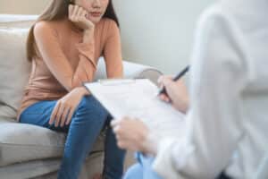 A young woman sits as a therapist takes notes.